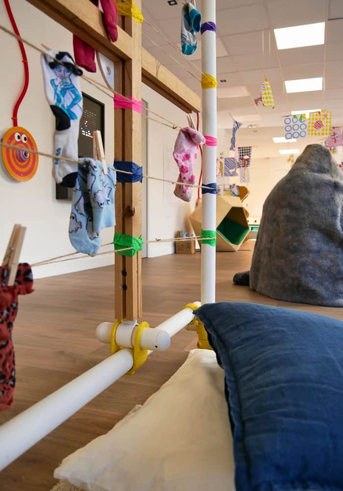 plusieurs chaussettes bleu et rose d'enfants suspendues dans la cabane a chaussettes orphelines, et des coussins en premier plan