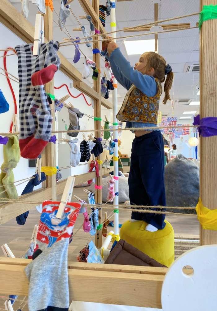 une enfant debout sur un tabouret qui attache une chaussettes orpheline dans la cabane à idées d'Hervé Tullet