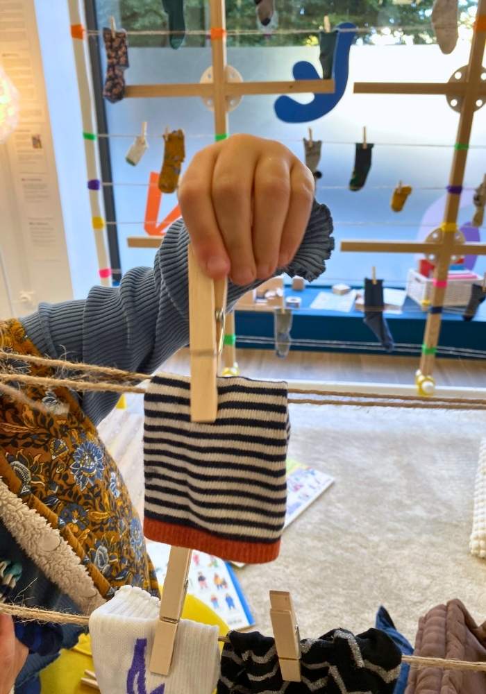 une main d'enfant qui accroche une chaussette orphelines sur la cabane d'Hervé Tullet avec une pince à linge
